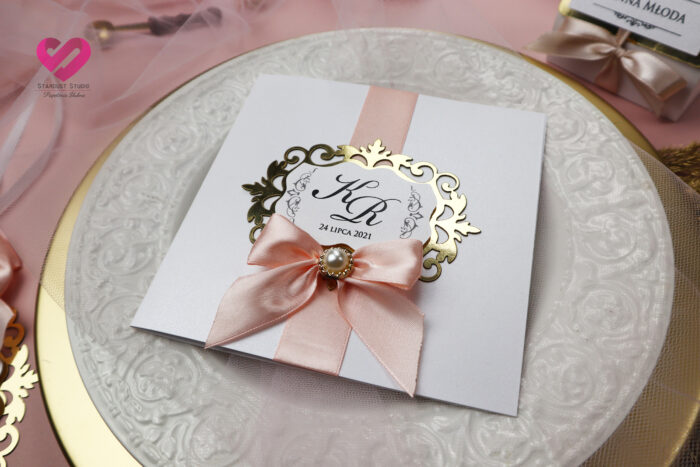 Pastelowe, romantyczne zaproszenia ślubne w stylu glamour z delikatną różową wstążką i złotym ażurem